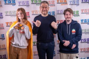 Trois personnes posant devant le photocall officiel du Toulouse Game Show avec logos TGS Montpellier, Pau, Toulouse, Perpignan et Lyon